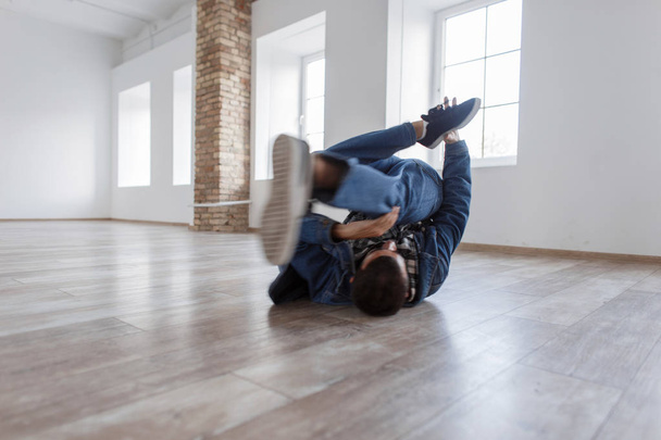 junger männlicher Tänzer in modischem Jeanskleid tanzt im Studio auf dem Boden - Foto, Bild