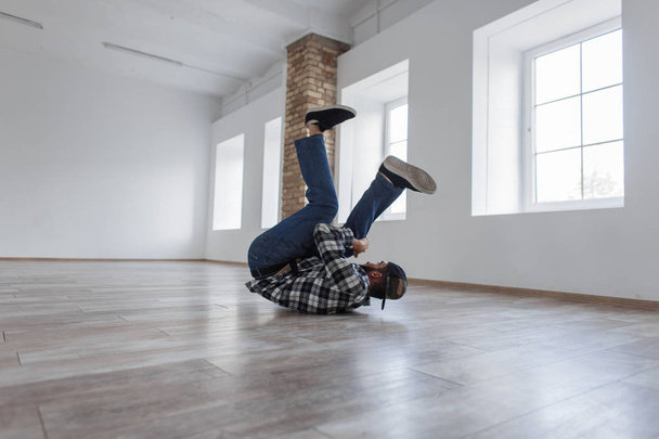 Stylový pohledný mladý muž s uzávěrem v košili s džíny tančící break dance v tanečním studiu - Fotografie, Obrázek