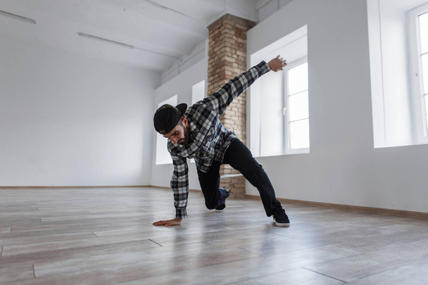 Young beautiful stylish dancer man with a cap and casual dress dancing break dance in the hall - Photo, Image