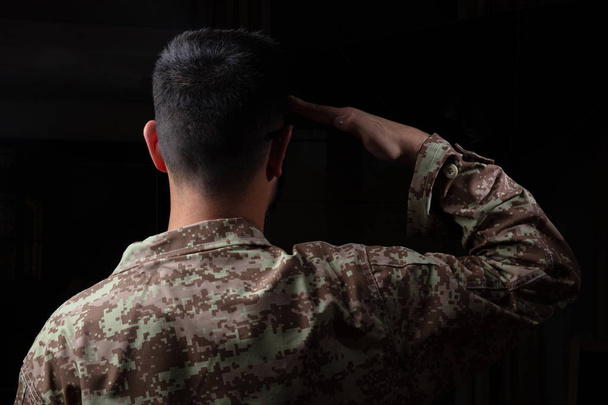 Нам армії. Молодий солдат, віддаючи честь стоячи на чорному фоні - Фото, зображення