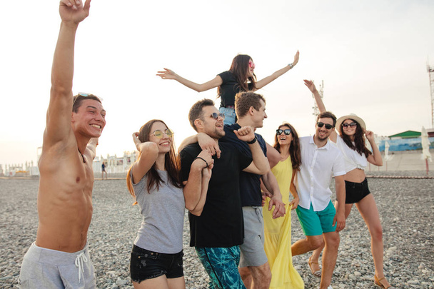Gruppo di amici che camminano in spiaggia, divertirsi, cavalcare le donne su uomini, vacanza divertente - Foto, immagini