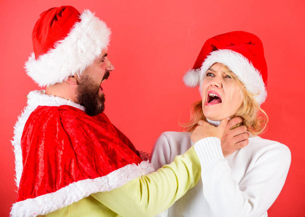 Couple celebrate winter holiday christmas. Christmas masquerade or karnival concept. Girl choking while man hold her neck celebrate christmas. Man with beard and woman in santa hat on red background - Фото, зображення