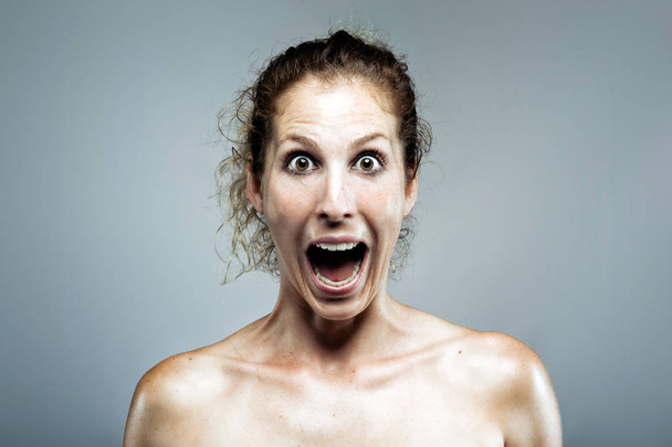 Portrait of beautiful young woman screaming while looking at camera over gray background. - Foto, Imagem