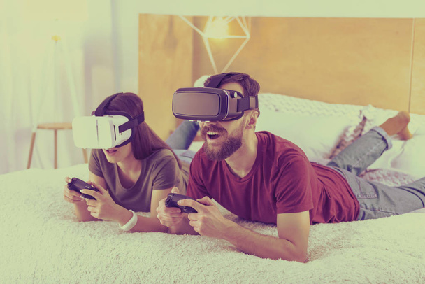 Nice couple in VR glasses laying on a bad - Foto, imagen