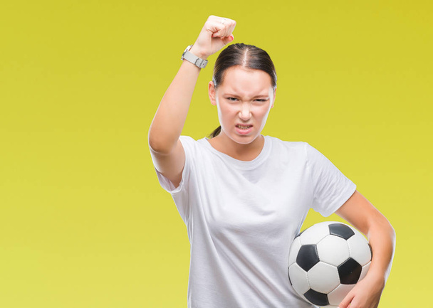 Молодая красивая белая женщина держит футбольный мяч на изолированном фоне раздраженный и разочарованный кричать от гнева, сумасшедший и кричать с поднятой рукой, гнев концепции
 - Фото, изображение