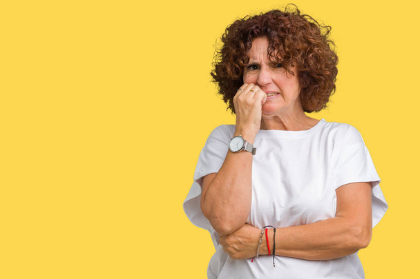 Krásné prostřední ager starší žena nosí bílé tričko izolované pozadí pohledu stresovaní a nervózní s rukama na ústech kousat nehty. Úzkost problem. - Fotografie, Obrázek