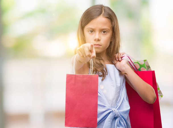 Brunette hispanic girl holding shopping bags pointing with finger to the camera and to you, hand sign, positive and confident gesture from the front - Fotografie, Obrázek