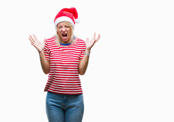 Young beautiful blonde woman wearing christmas hat over isolated background celebrating mad and crazy for success with arms raised and closed eyes screaming excited. Winner concept - Foto, Bild