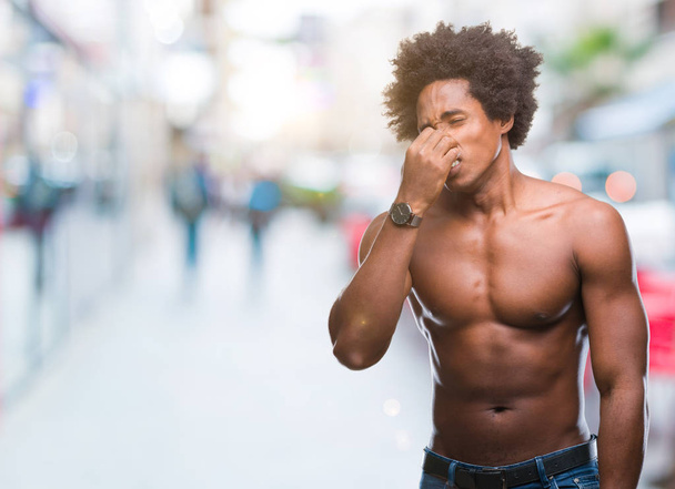 Afro americký shirtless muž ukazující nahé tělo nad izolované pozadí vonící něco smradlavá a nechutné, nesnesitelný zápach, držení dech s prsty na nos. Pachy koncept. - Fotografie, Obrázek