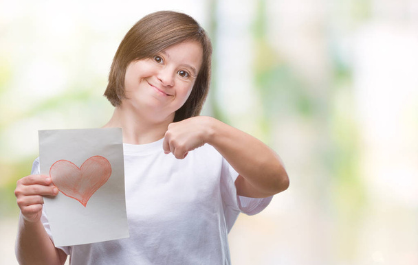 Young adult woman with down syndrome holding red heart card over isolated background with surprise face pointing finger to himself - Foto, Imagem