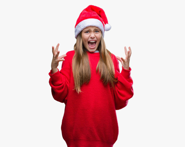 Üzerinde Noel şapka giyen genç güzel kız arka plan deli izole ve deli bağırarak ve agresif ifade ve silah kaldırdı bağırıyor. Hayal kırıklığı kavramı. - Fotoğraf, Görsel
