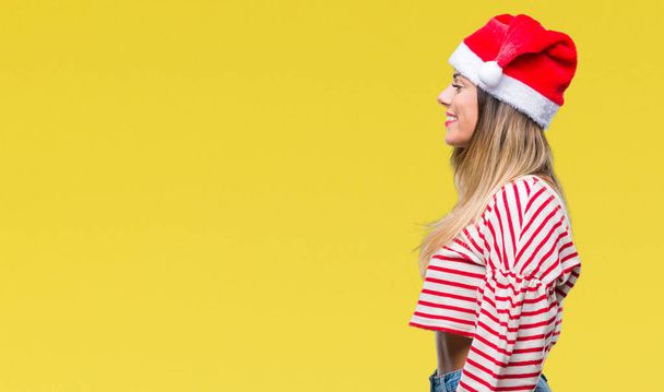 Молодая красивая женщина в рождественской шляпе на изолированном фоне глядя в сторону, расслабиться профиль позировать с естественным лицом с уверенной улыбкой
. - Фото, изображение