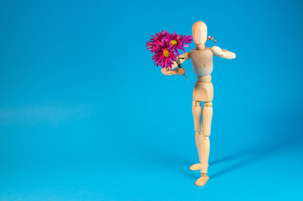 Wooden mannequin holding bouquet of flowers on blue background - Foto, imagen