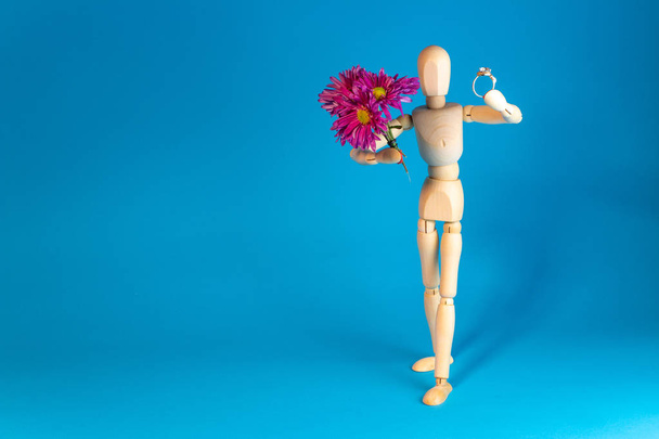 Wooden mannequin holding bouquet of flowers on blue background - Φωτογραφία, εικόνα