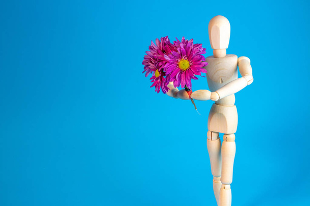 Wooden mannequin holding bouquet of flowers on blue background - Photo, image
