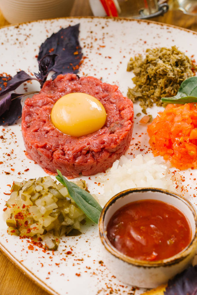 Vista cercana de la pasta de carne cruda con yema de huevo servida con verduras picadas en escabeche y salsa de tomate
  - Foto, Imagen