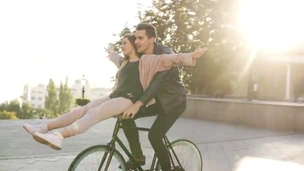 Joy and happiness of young couple have fun riding on the same bike in outdoor activity with sun backlight on the background. People, romance, leisure concept - Felvétel, videó
