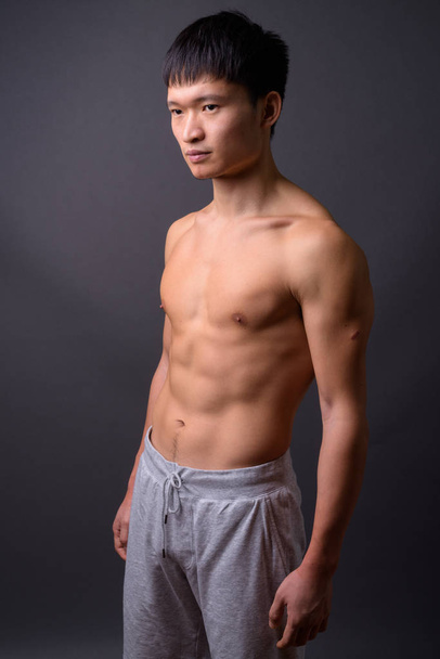 Jonge shirtloze Chinese man tegen grijze achtergrond - Foto, afbeelding