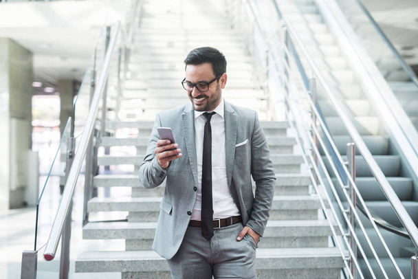 Young successful businessman going down the staircase and using smart phone for text message. - Photo, Image