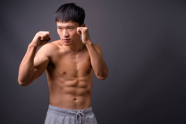 Jonge shirtloze Chinese man tegen grijze achtergrond - Foto, afbeelding