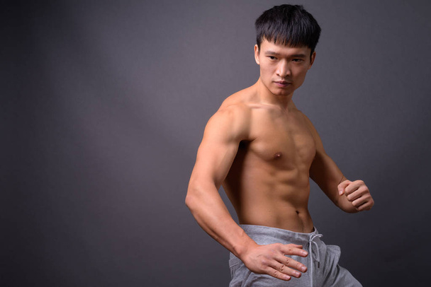 Студийный снимок молодого китайца без рубашки на сером фоне - Фото, изображение