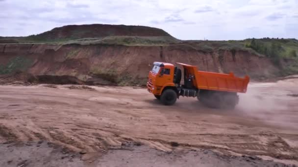 Άποψη του οδήγηση φορτηγό απορρίψεων σε αμμώδες έδαφος. Σκηνή. Πορτοκαλί ανατρεπόμενο φορτηγό βόλτες στο λατομείο με έδαφος στα πεδινά - Πλάνα, βίντεο