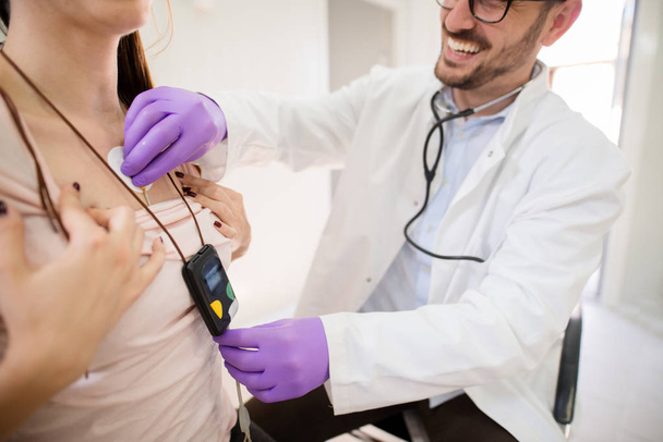 nuori nainen yllään Holter näytön laitteen kun lääkäri tarkistaa hänen terveydentilansa
 - Valokuva, kuva