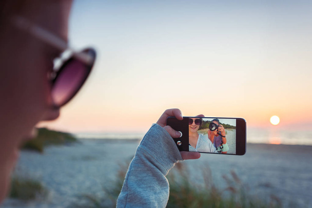 Mädchen machen Selfie vor spektakulärem Sonnenuntergang mit Handy  - Foto, Bild
