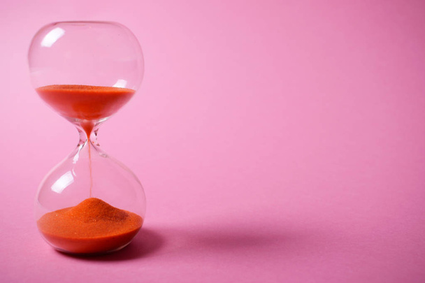 Reloj de arena naranja sobre fondo rosa
. - Foto, imagen