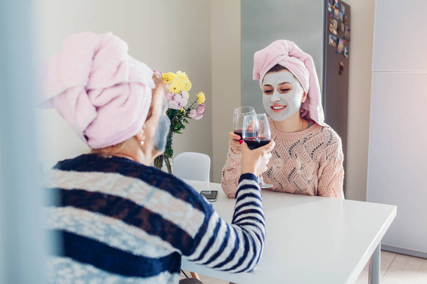 Anne ve yetişkin kızı uygulanan yüz maskeleri ile şarap içme. Soğutma ve mutfak konuşan kadın - Fotoğraf, Görsel