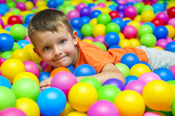 Onnellinen nauraa poika hauskaa pallo kuoppaan lasten huvipuisto ja leikkikeskus. Lapsi leikkii värikkäitä palloja leikkipaikka pallo allas
 - Valokuva, kuva