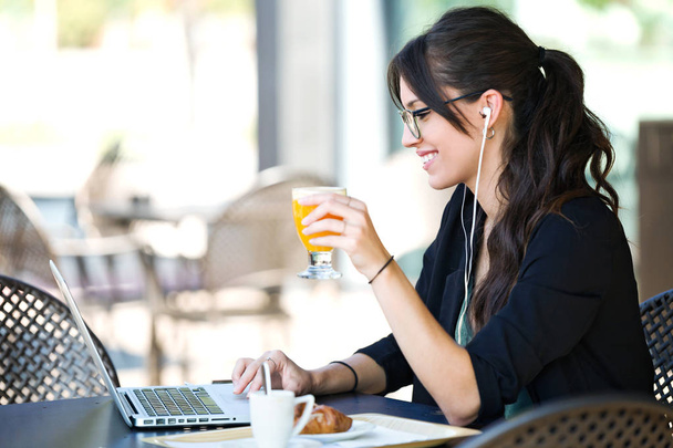 Lövés a gyönyörű fiatal nő iszik narancslé, miközben dolgozik rajta laptop a kávézóban. - Fotó, kép