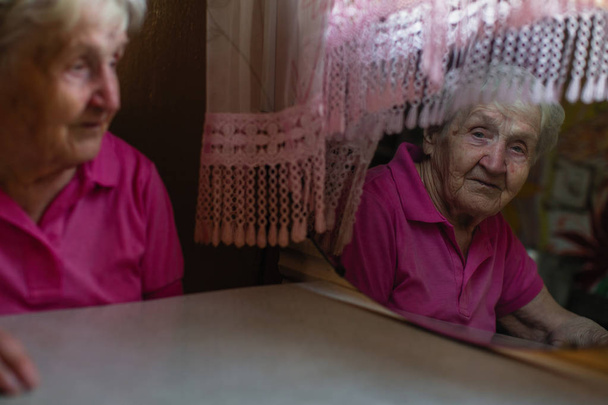 Uma mulher idosa olha através do reflexo no espelho
. - Foto, Imagem