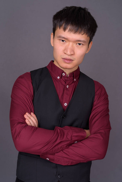Portrait of young Chinese businessman against gray background - 写真・画像