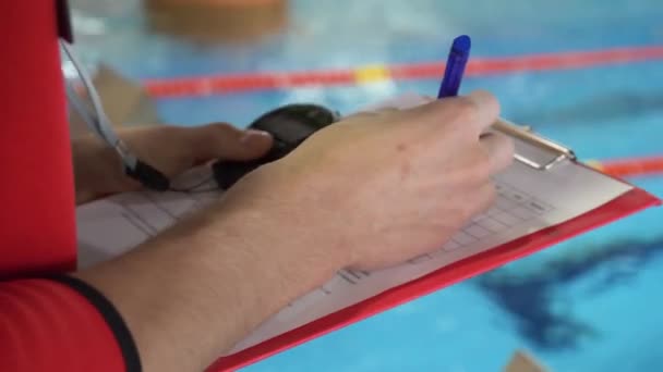 Sędzia w konkurencji w basenie. Zbliżenie dłoni sędziów w puli, który rejestruje zeznania w arkuszu - Materiał filmowy, wideo