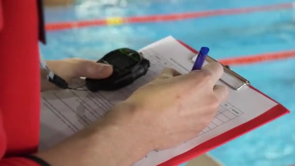 Juez en la competencia en la piscina. Primer plano de la mano de los jueces en la piscina que registra el testimonio en la hoja
 - Metraje, vídeo