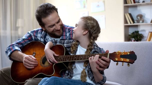 Father teaching daughter to play guitar at home, musical hobby, family leisure - Φωτογραφία, εικόνα