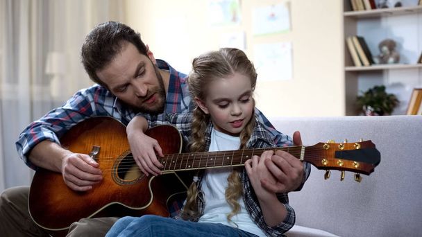 Caring dad teaching daughter to play guitar at home, musical hobby, family - Photo, image