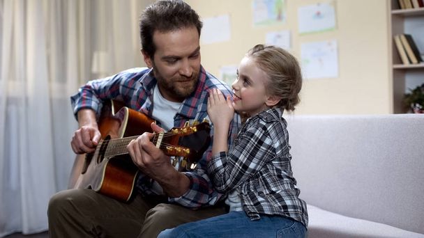 Tochter umarmt und hört Vater beim Gitarrespielen zu, Freizeit zusammen - Foto, Bild