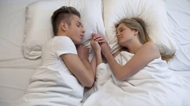 Couple stroking each other hands lying in bed, sweet moment before bedtime - Photo, image