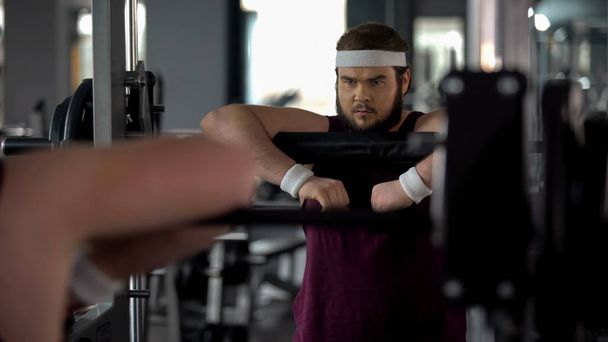 Purposeful chubby man posing at mirror as strong athlete, workout motivation - 写真・画像