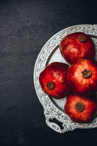flat lay with fresh pomegranates on metal serving tray on black tabletop - Foto, Imagen