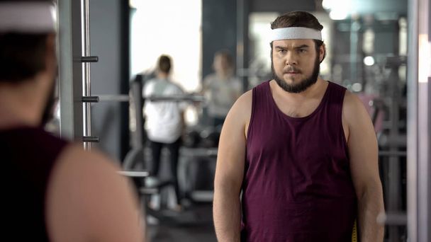 Fat man looking at mirror reflection in gym, mental training before workout - Photo, Image