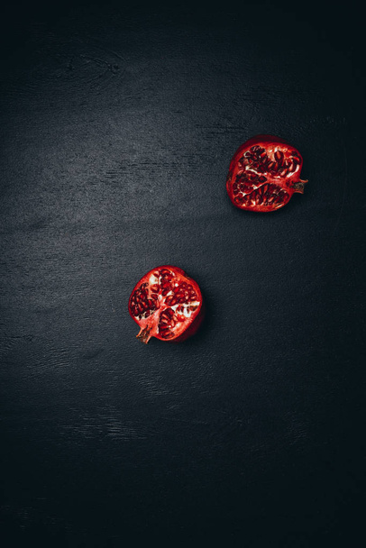 top view of pomegranate halves on black surface - Foto, Imagen