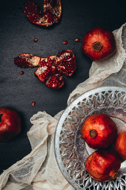 food composition with ripe and fresh pomegranates, metal bowl and gauze on black tabletop - Foto, imagen