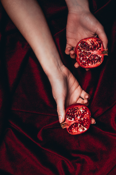 cropped shot of woman holding ripe pomegranate pieces on red velour fabric background - Foto, imagen