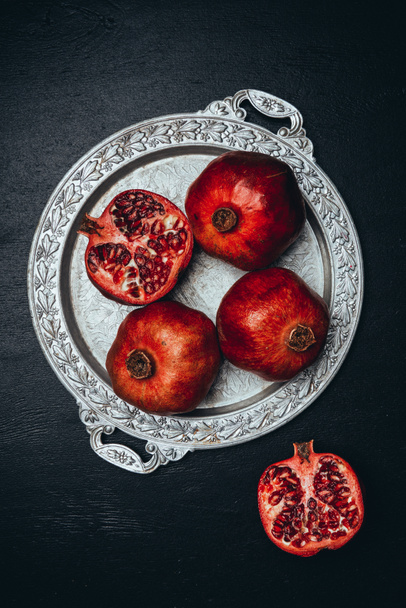flat lay with fresh pomegranates on metal serving tray on black tabletop - Foto, immagini