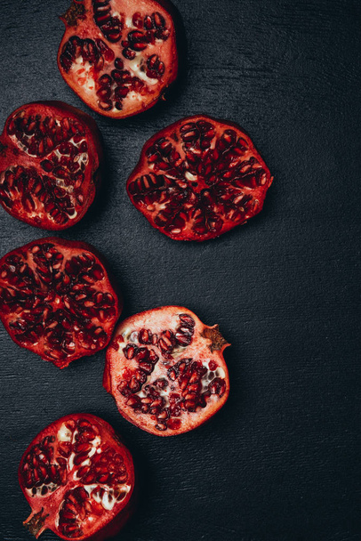 top view of cut pomegranates halves arrangement on black surface - Fotó, kép