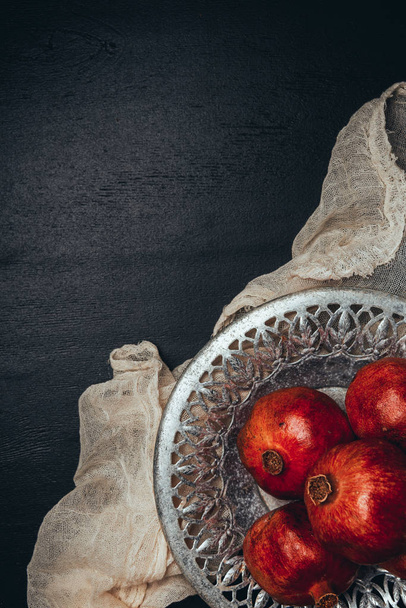 food composition with ripe and fresh pomegranates, metal bowl and gauze on black tabletop - Foto, immagini