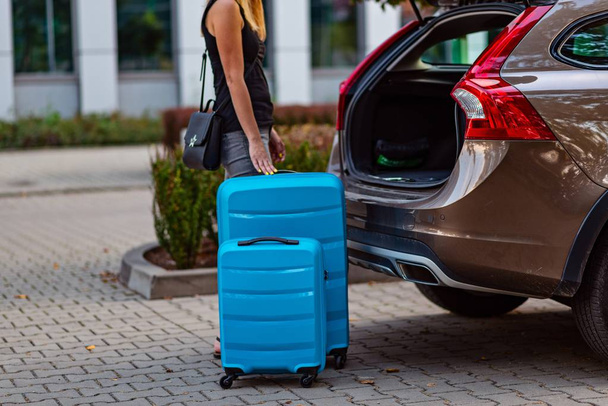 Mujer poniendo dos maletas de plástico azul en el maletero del coche. Preparación para el viaje
 - Foto, Imagen
